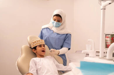 ولد عربي خليجي عماني يرتدي الزي العماني التقليدي  يجلس على كرسي العلاج في العيادة السنية،مفهوم الطب والرعاية الصحية، استخدام المعدات اللازمة لجراحة الاسنان ، طبيبة ترتدي القفازات تقوم بفحص أسنان المريض،  تقديم الخدمات الطبية للمرضى ، إجراء الفحوصات الدورية للعناية بالصحة الفموية