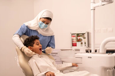 مفهوم الطب والرعاية الصحية، استخدام المعدات اللازمة لجراحة الاسنان ، طبيبة ترتدي القفازات تقوم بفحص أسنان المريض، ولد عربي خليجي عماني يرتدي الزي العماني التقليدي يجلس على كرسي العلاج في العيادة السنية، تقديم الخدمات الطبية للمرضى ، إجراء الفحوصات الدورية للعناية بالصحة الفموية