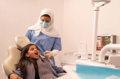 بنت عربية خليجية عمانية ترتدي الزي الكاجوال تجلس على كرسي العلاج في العيادة السنية، استخدام المعدات اللازمة لجراحة الاسنان ، مفهوم الطب والرعاية الصحية، طبيبة ترتدي القفازات تقوم بفحص أسنان المريض،تقديم الخدمات الطبية للمرضى ، إجراء الفحوصات الدورية للعناية بالصحة الفموية