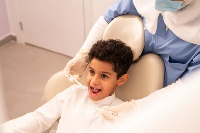 A female doctor wearing gloves is examining the patient's teeth, using the necessary equipment for dental surgery, the concept of medicine and healthcare, an Arab Gulf Omani boy wearing traditional Omani attire is sitting on the treatment chair in the dental clinic, providing medical services to patients, conducting regular check-ups for oral health care.