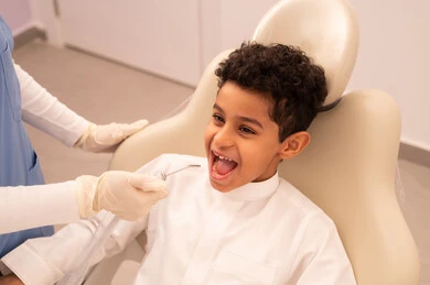 مفهوم الطب والرعاية الصحية، استخدام المعدات اللازمة لجراحة الاسنان ، طبيبة ترتدي القفازات تقوم بفحص أسنان المريض، ولد عربي خليجي عماني يرتدي الزي العماني التقليدي  يجلس على كرسي العلاج في العيادة السنية، تقديم الخدمات الطبية للمرضى ، إجراء الفحوصات الدورية للعناية بالصحة الفموية