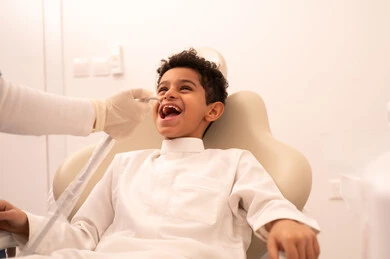 استخدام المعدات اللازمة لجراحة الاسنان ، مفهوم الطب والرعاية الصحية، طبيبة ترتدي القفازات تقوم بفحص أسنان المريض، ولد عربي خليجي عماني يرتدي الزي العماني التقليدي  يجلس على كرسي العلاج في العيادة السنية، تقديم الخدمات الطبية للمرضى ، إجراء الفحوصات الدورية للعناية بالصحة الفموية