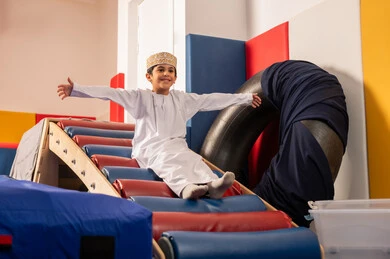 العاب التسلية والمتعه، الاستمتاع بالالعاب الترفيهية، ولد عربي خليجي عماني يرتدي الدشداشه والكمه مستمتع بالتزحلق على الزحليقة ، مدينه الالعاب في سلطنة عمان ، مفهوم اللهو واللعب، اجواء صيفية ممتعة