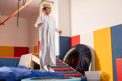 العاب التسلية والمتعه، ولد عربي خليجي عماني يرتدي الزي التقليدي مستمتع باللعب امام  الزحليقة ، الاستمتاع بالالعاب الترفيهية، مدينه الالعاب في سلطنة عمان ، مفهوم اللهو واللعب، اجواء صيفية ممتعة،