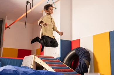 Entertainment and fun games, enjoyable summer atmosphere, amusement park in the Sultanate of Oman, the concept of play and leisure, jumping high with gestures of happiness and joy, an Arab Gulf Omani boy wearing casual attire enjoying playing in front of the slide, enjoying recreational games.