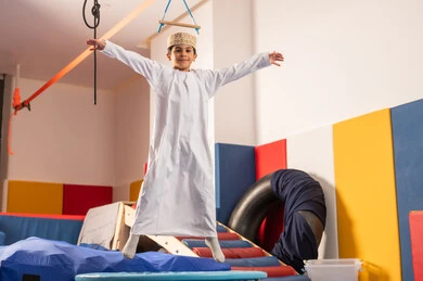 الاستمتاع بالالعاب الترفيهية، اجواء صيفية ممتعة، مدينه الالعاب في سلطنة عمان، مفهوم اللهو واللعب، القفز عالياً بايماءات السعادة والسرور،ولد عربي خليجي عماني يرتدي الدشداشه والكمه مستمتع باللعب امام الزحليقة ،  العاب التسلية والمتعه