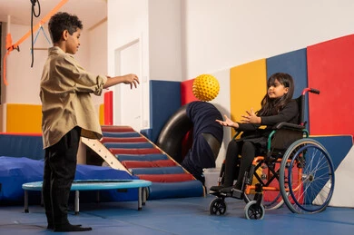 رياض الأطفال والحاضنات، بنت عمانية تجلس على كرسي متحرك تلعب بالكره فى مدينة الالعاب برفقة ولد سعودي، أداء الكثير من الأنشطة الممتعة لذوي الهمم، الاعتناء بالاطفال ذوي الاحتياجات الخاصة