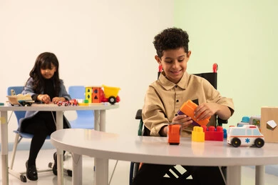 Developing mental and intellectual skills, performing many fun activities for people of determination, caring for children with special needs, kindergartens and nurseries, an Omani Gulf Arab girl wearing casual attire engaging in skills and activities, a Saudi boy playing with colored blocks.