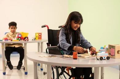 An Omani Gulf Arab girl wearing casual attire is engaged in skills and activities, kindergartens and nurseries, performing many fun activities for people with determination, taking care of children with special needs, and a Saudi boy playing with colorful plastic toys.