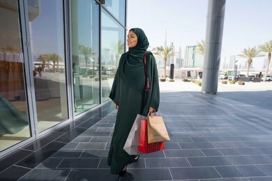 Shopping obsession in the Gulf community, a veiled Emirati Gulf Arab woman wearing an abaya carrying paper bags, taking advantage of seasonal offers and discounts and White Friday, shopping from malls, gestures of happiness and pleasure