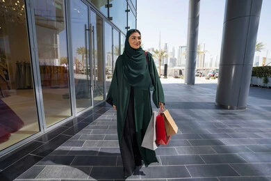 الترويج لماركات عالمية فاخرة، إمرأة عربية خليجية اماراتية محجبة ترتدي العباءه تحمل بيدها أكياس ورقية, استغلال العروض والتخفيضات الموسمية والجمعة البيضاء، التسوق من المولات التجارية، ايماءات السعاده و السرور