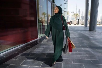 Choosing things and supplies from shopping malls, a veiled Emirati Gulf Arab woman wearing an abaya holding paper bags, taking advantage of seasonal offers and discounts and White Friday, shopping from shopping malls, gestures of happiness and pleasure