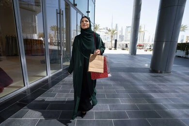ايماءات السعاده و السرور، متعة الشراء من الماركات العالمية، إمرأة عربية خليجية اماراتية محجبة ترتدي العباءه تحمل بيدها أكياس ورقية, استغلال العروض والتخفيضات الموسمية والجمعة البيضاء، التسوق من المولات التجارية