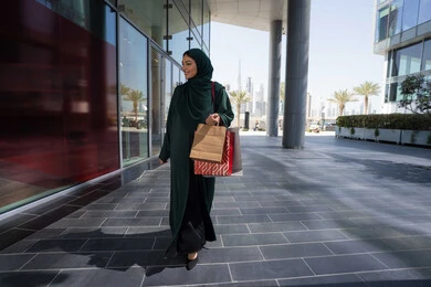Shopping in malls, buying and taking necessary supplies, a veiled Emirati Gulf Arab woman wearing an abaya, carrying paper bags, taking advantage of seasonal offers and discounts and White Friday, gestures of happiness and pleasure