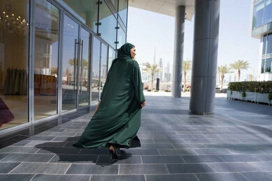 Enjoy shopping, a picture from the back of an Emirati Gulf Arab woman wearing an abaya, carrying shopping bags in her hands, facial expressions indicating happiness, having a good time buying supplies, taking advantage of offers and discounts, a background outside the mall