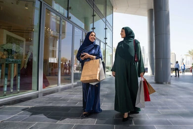 شراء الحاجات من المول، اختيار المستلزمات والهدايا برفقة الأصدقاء ،امراتان عربيتان خليجيتان اماراتيان يرتديان العباءه و الحجاب تمسكان بالأكياس الورقية يتسوقان بإيماءات البشاشة والحماس