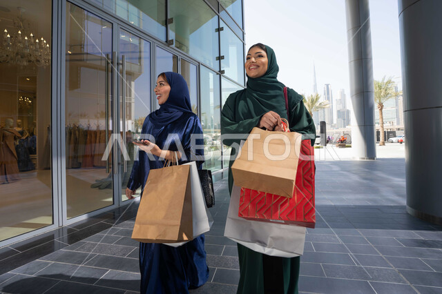 متعة التسوق في الامارات العربية ، الجمعه البيضاء، الشراء في أيام التنزيلات والتخفيضات، الاستمتاع بالشراء والتسوق ، التسوق مع الاصدقاء، سيدتان عربيتان خليجيتان اماراتيان ترتديان العباءه و الحجاب تحملان حقائب التسوق