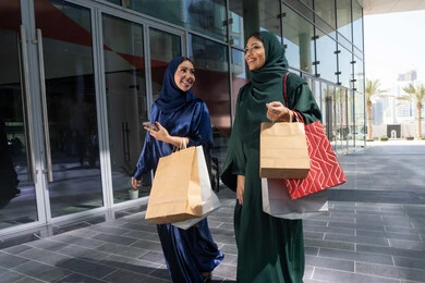 Buying necessities and gifts, the pleasure of shopping with friends, two Emirati Gulf Arab women wearing abaya and hijab carrying shopping bags, shopping during sales and reductions days, White Friday