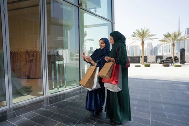 The joy of shopping with friends, using a mobile phone, gestures and facial expressions indicating happiness, two Emirati Gulf Arab women carrying shopping bags, shopping during sales and reductions days, White Friday