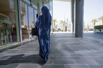 استغلال الخصومات والتنزيلات، توثيق اللحظات السعيدة، استخدام الأجهزة والتقنيات المتطورة، إمرأة سعودية تقوم بالتسوق وشراء المستلزمات والهدايا،صورة من الخلف سيدة عربية خليجية اماراتية ترتدي الحجاب والعباءة تمسك بيدها الهاتف المحمول وأكياس التسوق