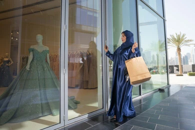 تعابير السرور والسعادة، مفهوم التسوق واقتناء الهدايا، استخدام التكنولوجيا في الحياة اليومية، إمرأة سعودية تقوم بالتسوق وشراء المستلزمات، سيدة عربية خليجية اماراتية ترتدي الحجاب والعباءة تمسك بيدها الهاتف المحمول وأكياس التسوق و تقوم بتصوير فتان اخضرداخل متجر