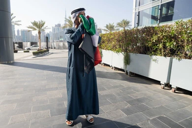 حب الوطن والعلم، الإحتفال باليوم الوطني الإمارات، التجول في الهواء الطلق، هوية اليوم الوطني الاماراتي 2 ديسمبر، اليوم الوطني الاماراتي 1971، رجل عربي خليجي اماراتي يرتدي الكندرة الغترة التقليدية يقبل علم الامارات العربية المتحدة في النهار، الجسم بالطول الكامل
