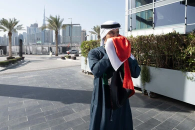 الإحتفال باليوم الوطني الإمارات، التجول في الهواء الطلق، هوية اليوم الوطني الاماراتي 2 ديسمبر، اليوم الوطني الاماراتي 1971، رجل عربي خليجي اماراتي يرتدي الكندرة الغترة التقليدية يقبل علم الامارات العربية المتحدة في النهار، حب الوطن والاعتزاز به