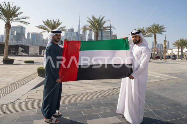 الإحتفال باليوم الوطني الإماراتي، يوم استقلال الإمارات، رجلان عربيان خليجيان اماراتيان يرتديان الكندورة والغترة يحملان علم الإمارات العربية المتحدة، الاعتزاز والفخر بإنجازات البلاد، هوية اليوم الوطني الاماراتي 51، الطول الكامل للجسم
