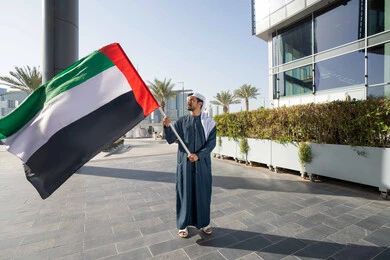 إيماءات الاعتزاز والفخر، مفهوم حب الوطن والانتماء إليه، إحياء ذكرى استقلال البلاد، رجل عربي خليجي إماراتي يرتدي الكندورة والغترة يرفع علم الإمارات المتحدة، الاحتفال باليوم الوطني 2 ديسمبر، الجسم بالطول الكامل