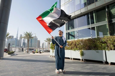 التجول في الشوارع بايماءات السعادة والفخر والاعتزاز، إحياء ذكرى استقلال البلاد، مفهوم حب الوطن والانتماء إليه، رجل عربي خليجي إماراتي يرتدي الكندورة والغترة يرفع علم الإمارات المتحدة، الاحتفال باليوم الوطني 2 ديسمبر، الجسم بالطول الكامل