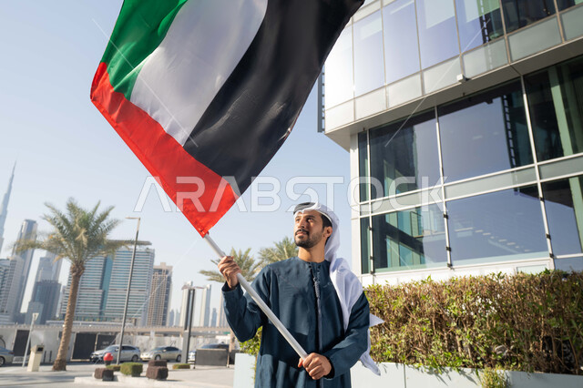 إحياء ذكرى استقلال البلاد، مفهوم حب الوطن والانتماء إليه، صورة مقربة لرجل عربي خليجي إماراتي يرتدي الكندورة والغترة يرفع علم الإمارات المتحدة، الاحتفال باليوم الوطني 2 ديسمبر، إيماءات الاعتزاز والفخر