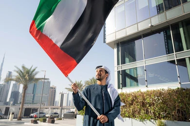إحياء ذكرى استقلال البلاد، مفهوم حب الوطن والانتماء إليه، صورة مقربة لرجل عربي خليجي إماراتي يرتدي الكندورة والغترة يرفع علم الإمارات المتحدة، الاحتفال باليوم الوطني 2 ديسمبر، إيماءات الاعتزاز والفخر