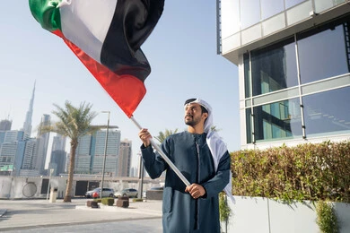 مفهوم حب الوطن والانتماء إليه، إحياء ذكرى استقلال البلاد، رجل عربي خليجي إماراتي يرتدي الكندورة والغترة يرفع علم الإمارات المتحدة، الاحتفال باليوم الوطني 2 ديسمبر، إيماءات الاعتزاز والفخر