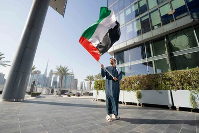 Commemorating the country's independence, the concept of patriotism and belonging to the homeland, an Emirati Gulf Arab man wearing a kandura and ghutra raising the flag of the United Arab Emirates, celebrating the National Day on December 2, gestures of pride and honor, a full-length body image