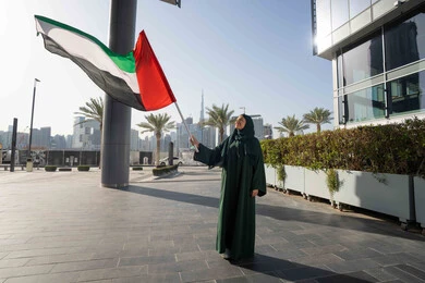 Remembering the UAE National Day 1971, walking in the streets with gestures of happiness, pride and honor, the anniversary of the founding of the Union, December 2, an Arab Gulf Emirati woman wearing a hijab and abaya holding the flag of the United Arab Emirates, Flag Day, November 3, love of the homeland and pride in it