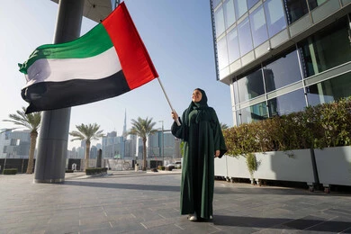 التجول في الشوارع بايماءات السعادة والفخر والاعتزاز، ذكرى تأسيس الاتحاد 2 ديسمبر،استذكار اليوم الوطني الاماراتي 1971، إمراة عربية خليجية إماراتية ترتدي الحجاب والعباءة تمسك بيدها علم الإمارات العربية المتحدة ، يوم العلم 3 نوفمبر، حب الوطن والاعتزاز به