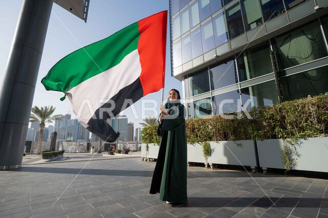 استذكار اليوم الوطني الاماراتي 1971، ذكرى تأسيس الاتحاد 2 ديسمبر، إمراة عربية خليجية إماراتية ترتدي الحجاب والعباءة تمسك بيدها علم الإمارات العربية المتحدة ، يوم العلم 3 نوفمبر، حب الوطن والاعتزاز به، التجول في الشوارع بايماءات السعادة والفخر والاعتزاز