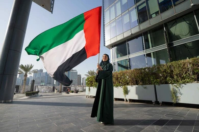 Commemorating the UAE National Day 1971, the anniversary of the founding of the Union, December 2, an Emirati Gulf Arab woman wearing a hijab and abaya holding the UAE flag in her hand, Flag Day, November 3, love of the homeland and pride in it, walking in the streets with gestures of happiness, pride and pride