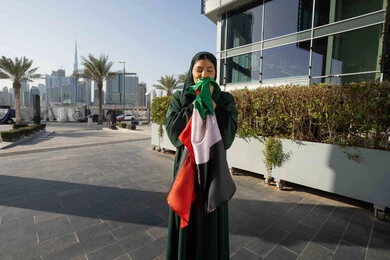 مفهوم حب الوطن والانتماء اليه، احياء اليوم الوطني الإماراتي 2 ديسمبر، الاحتفال بذكرى استقلال دولة الإمارات العربية المتحدة، امراة عربية خليجية اماراتية ترتدي العباءة والحجاب تقبل علم الإمارات في النهار، التجول في الشوارع بايماءات السعادة والفخر والاعتزاز