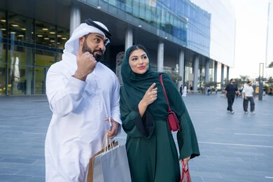 Having a great time shopping, having fun at the mall, an Emirati Gulf Arab couple wearing traditional clothes carrying colorful shopping bags, shopping and buying necessities from malls in the UAE, White Friday offers