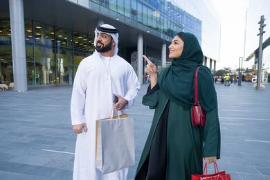 The joy of shopping in the mall, an Emirati Gulf Arab couple wearing traditional dress carrying colorful shopping bags, shopping and buying supplies from shopping malls in the UAE, White Friday offers