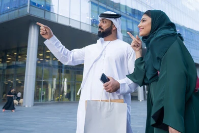 Shopping during discounts and sales, taking advantage of seasonal offers and discounts, an Emirati Gulf Arab couple wearing traditional dress carrying colorful shopping bags, shopping and buying supplies from shopping malls in the United Arab Emirates