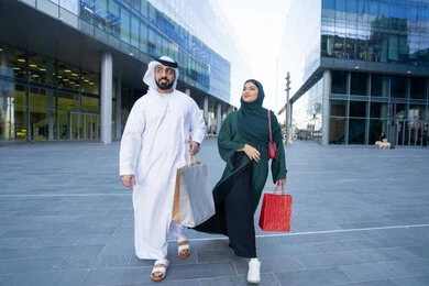 الأناقة والاهتمام بالمظهر الخارجي، الاستفادة من العروض الموسمية والتخفيضات، زوجان عربيان خليجيان اماراتيان يرتديان الزي التقليدي يحملان اكياس التسوق الملونه، التبضع وشراء المستلزمات من المولات التجارية في الامارت العربية، الجسم بالطول الكامل