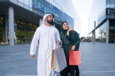 Black Friday offers, shopping and buying supplies from malls in the UAE, taking advantage of seasonal offers and discounts, an Emirati Gulf Arab couple wearing traditional dress carrying colorful shopping bags