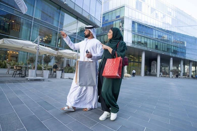 Taking advantage of seasonal offers and discounts, an Emirati Gulf Arab couple wearing traditional dress carrying colorful shopping bags, shopping and buying supplies from shopping malls in the UAE, White Friday offers