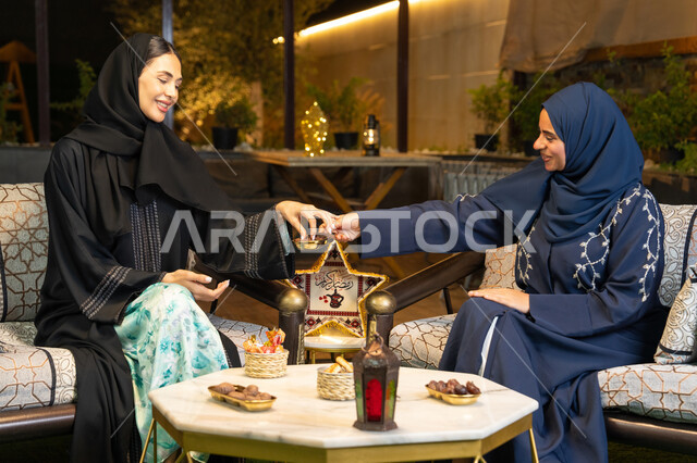 زينة واضاءة رمضانية،  حسن الاستقبال في شهر رمضان المبارك، امراتان سعوديتان تجلسان بالجلسة الخارجية في احدى شاليهات الامارات، صديقتان عربيتان خليجيتان اماراتيتان ترتديان العباءة والحجاب تجلسان في الهواء الطلق