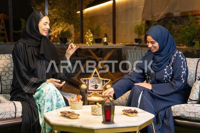 A local Emirati product, eating fresh sugar dates, a warm welcome during the holy month of Ramadan, Ramadan decorations and lighting, two Saudi women sitting outdoors in a chalet in the Emirates, two Emirati Gulf Arab friends wearing the abaya sitting outdoors