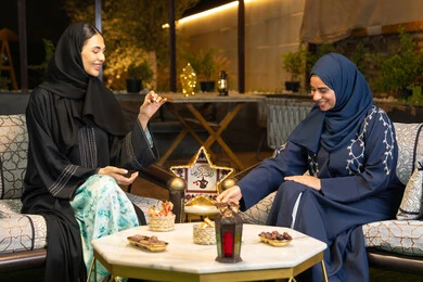 منتج وطني محلي اماراتي،  تناول التمر السكري الطازج، حسن الاستقبال في شهر رمضان المبارك، زينة واضاءة رمضانية، امراتان سعوديتان تجلسان بالجلسة الخارجية في احدى شاليهات الامارات، صديقتان عربيتان خليجيتان اماراتيتان ترتديان العباءة تجلسان في الهواء الطلق