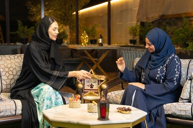 Warm welcome in the holy month of Ramadan, Ramadan decorations and lighting, two Saudi women sitting outdoors in a chalet in the Emirates, two Emirati Gulf Arab friends wearing the abaya sitting outdoors, a local Emirati product, eating fresh sugar dates