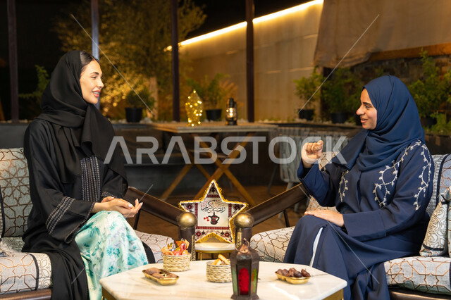 تناول التمر السكري الطازج، منتج وطني محلي اماراتي، حسن الاستقبال في شهر رمضان المبارك، زينة واضاءة رمضانية، امراتان سعوديتان تجلسان بالجلسة الخارجية في احدى شاليهات الامارات، صديقتان عربيتان خليجيتان اماراتيتان ترتديان العباءة تجلسان في الهواء الطلق